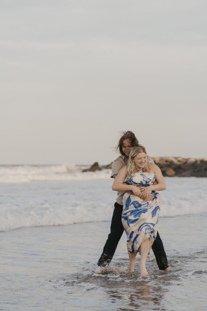 Cape Henlopen Beach (DE) engagement photo shoot where the couple is standing in shallow water on beach
